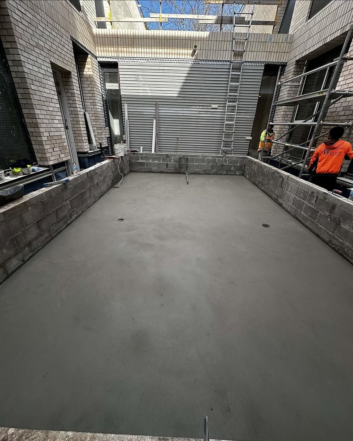 A broad finished screed surface across a Melbourne courtyard, with the real worksite visible around it